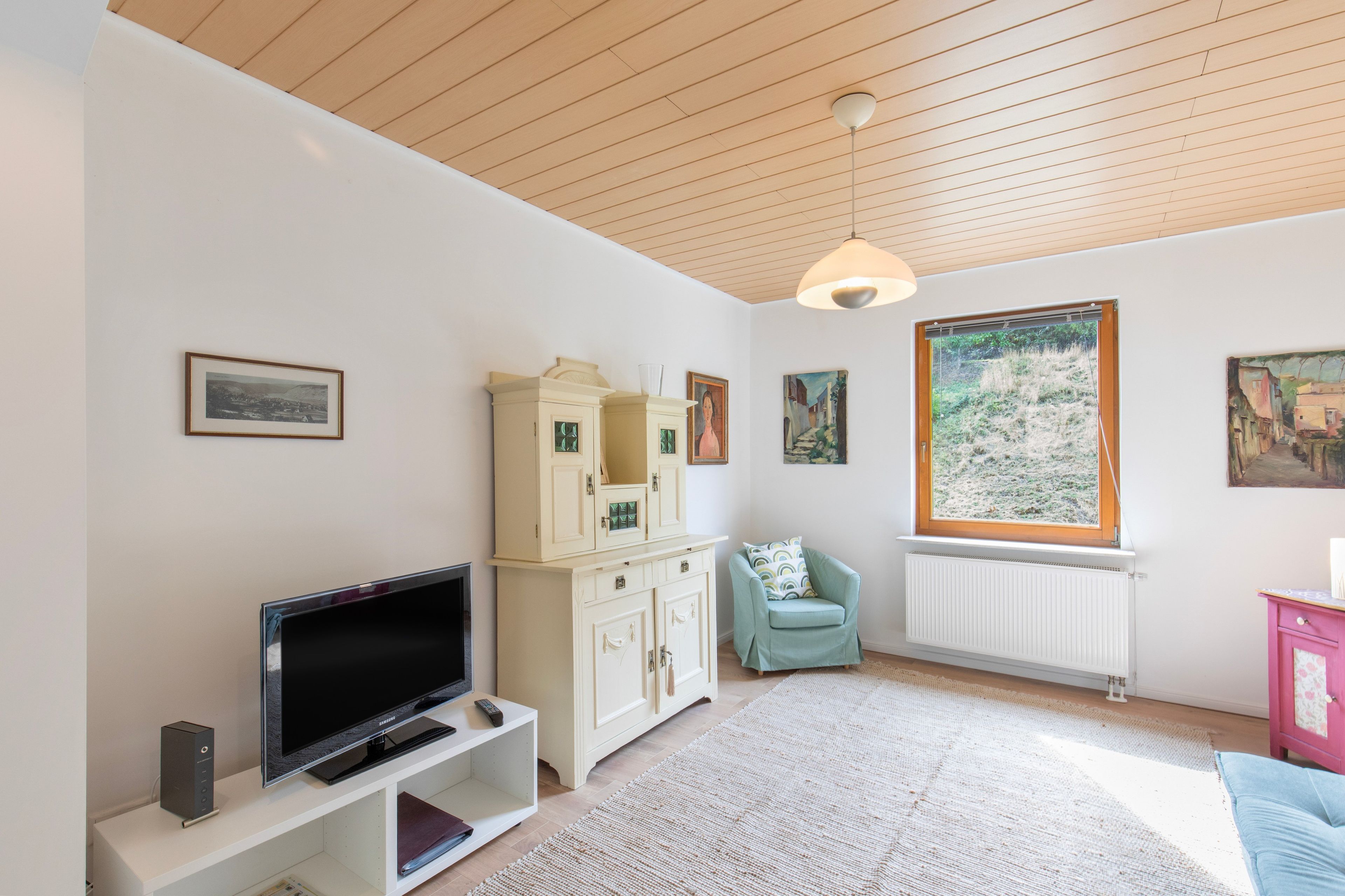 A living room with a television, cabinets, a chair, and artwork on the walls.