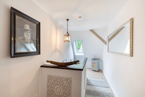 A hallway with a wooden boat sculpture, a framed picture, a hanging light fixture, and a mirror on the wall.