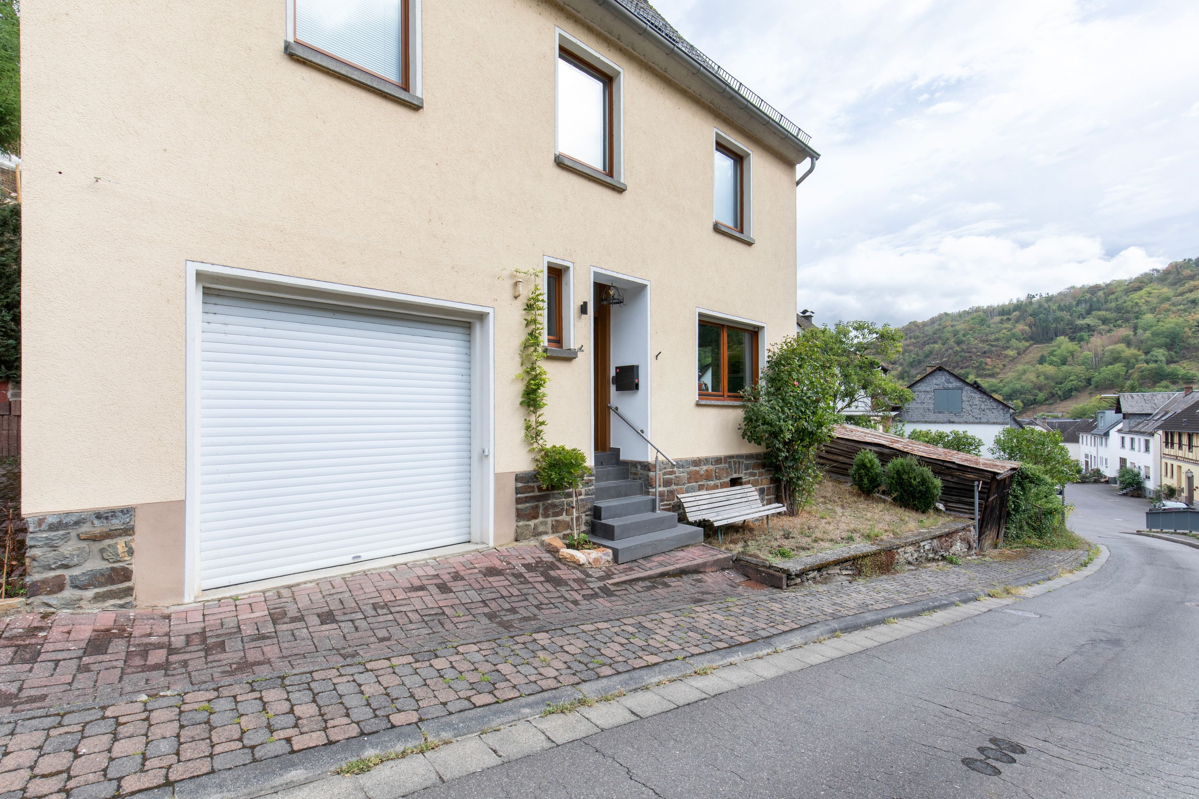 Ein zweistöckiges Haus mit Garage, einer Veranda mit Bank und einem Steinfundament.