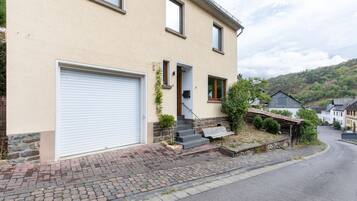 Ein zweistöckiges Haus mit Garage, einer Veranda mit Bank und einem Steinfundament.