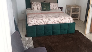 Un dormitorio con una cama, una silla, un estante de madera y un aire acondicionado de pared.
