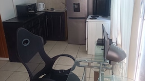 Cocina compacta con refrigerador, microondas y una pequeña zona de comedor con una silla y mesa.