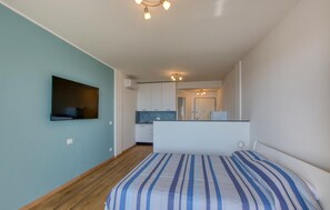 A bedroom with a bed, a TV mounted on the wall, a kitchen area with cabinets, and a ceiling light fixture. - Stunning apartment in Recco with WiFi (Recco)