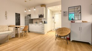 Eine moderne Küche mit weißen Schränken, ein Essbereich mit einem Holztisch und Stühlen sowie ein Korbstuhl.