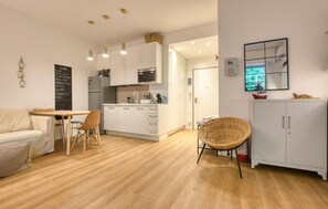 A modern kitchen with white cabinets, a dining area with a wooden table and chairs, and a wicker chair. - Gorgeous apartment in Rapallo with WiFi (Rapallo)