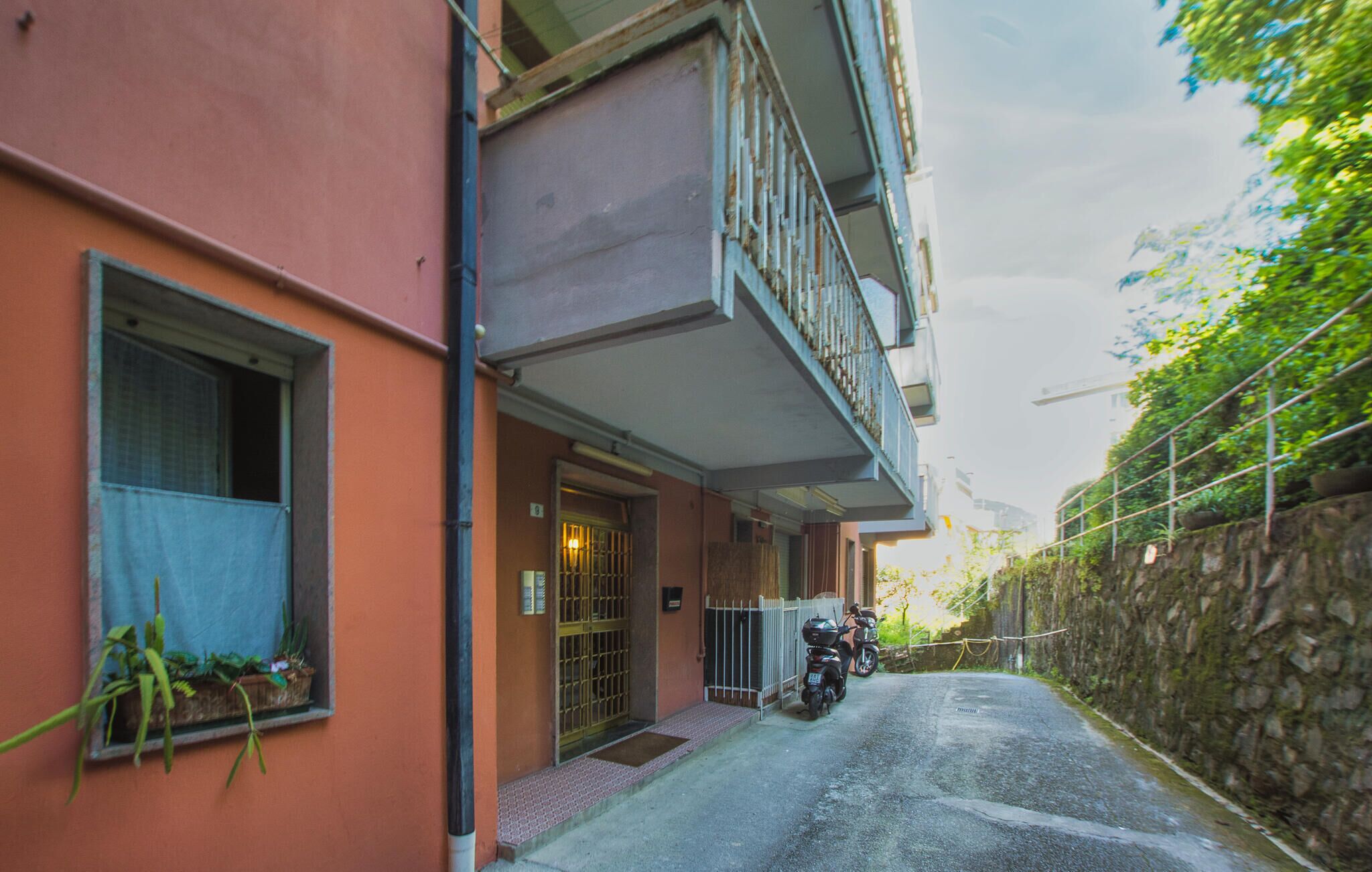 A narrow street with a building on the left, a gated entrance, and a motorcycle parked in front.