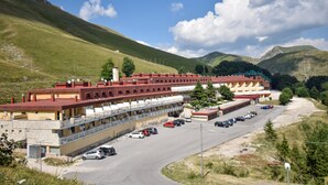 Ein mehrstöckiges Hotel mit Parkplatz, gelegen in einer hügeligen Landschaft mit Bergen im Hintergrund.