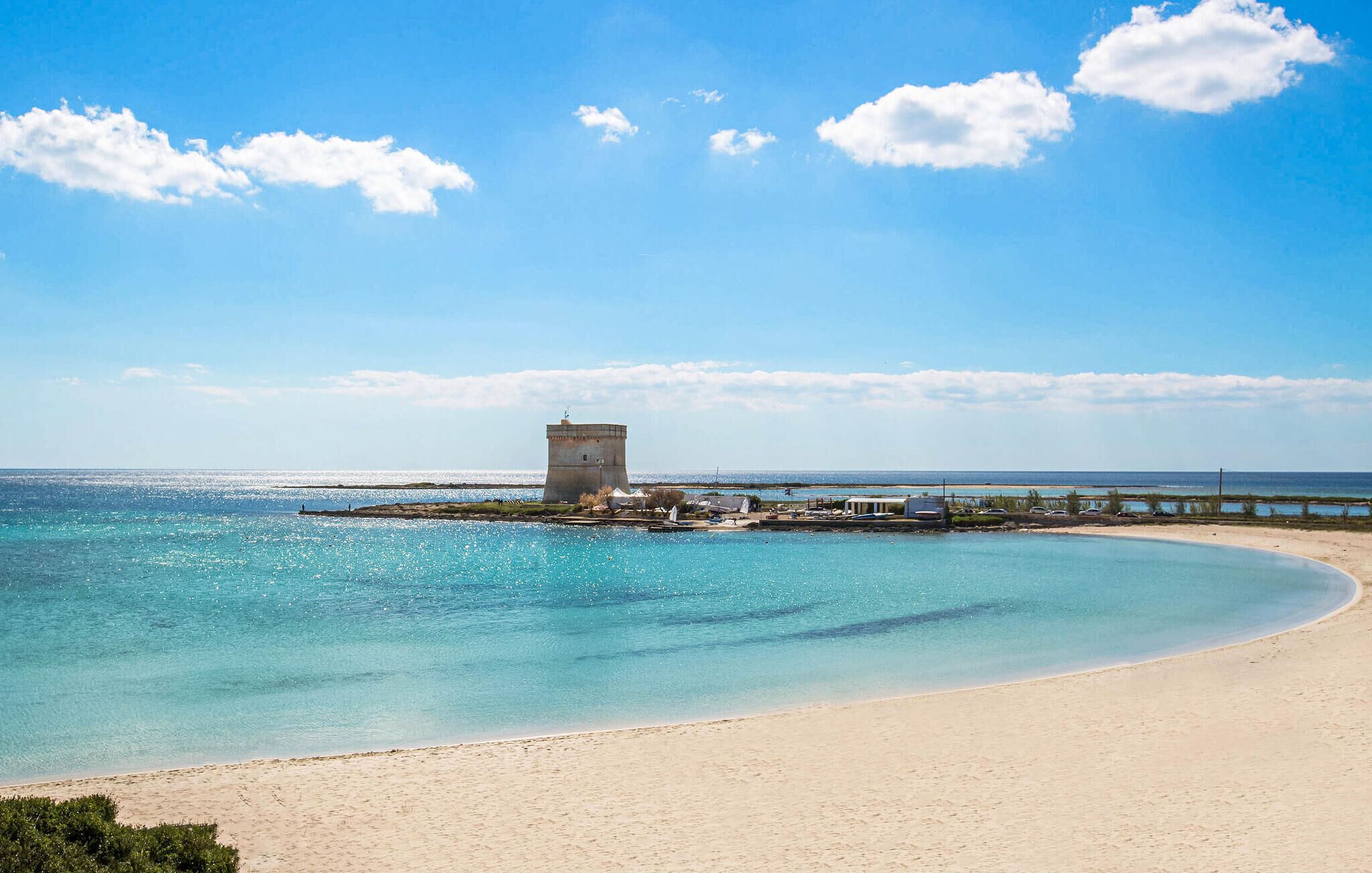 A beach with clear turquoise water, a sandy shore, and a small tower structure.