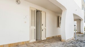 Um edifício com fachada branca, duas portas com portões e entrada em pedra, sob um céu claro.
