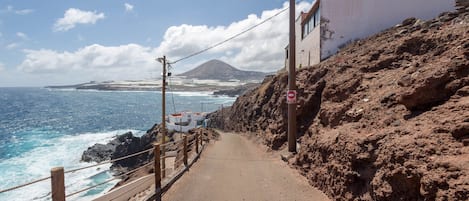 Una carretera costera con una ladera rocosa, cielo despejado y vista al océano.