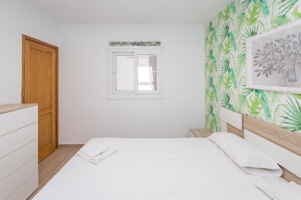 A bedroom with a bed, a wooden wardrobe, a window, and a wall with a leaf pattern.