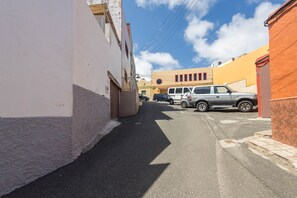 A narrow street with buildings on either side, a parked car, and a clear sky. - 2BR La Furnia Home - Balcony & Natural Pool (Gáldar)