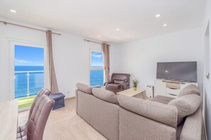A modern living room with a sofa, a television, and a view of the sea.