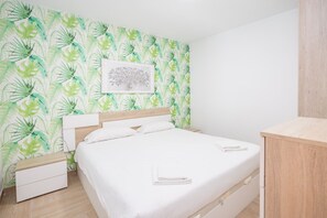 Une chambre à coucher comprenant un lit, une table de chevet, une tête de lit en bois et un mur orné d’un motif végétal.