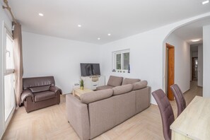 A modern living room with a sofa, a television, and a dining area.