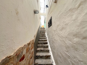 A narrow stairway leading upwards, flanked by white walls with a stone base.