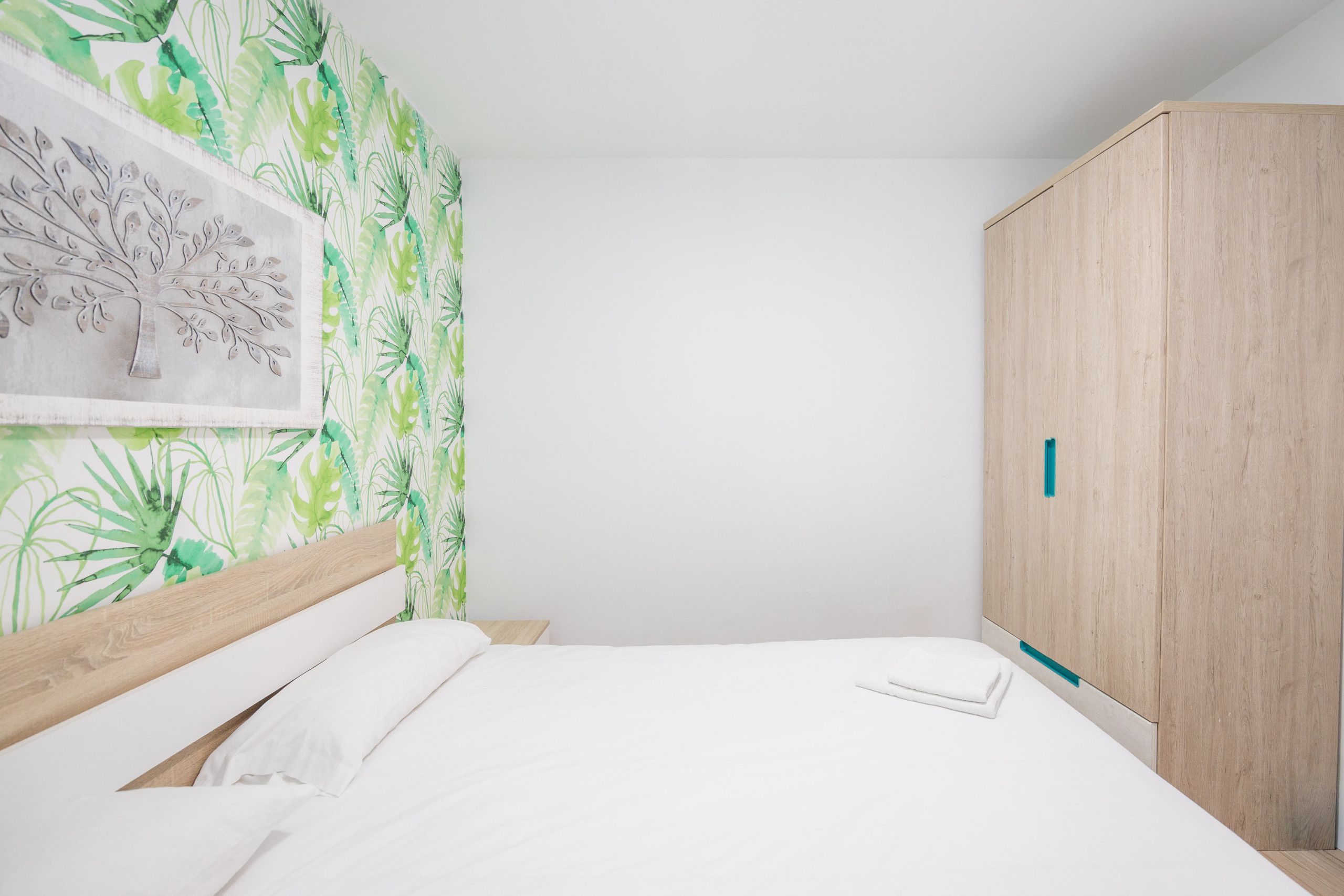 A bedroom with a bed, a wardrobe, and a wall with a leaf pattern.