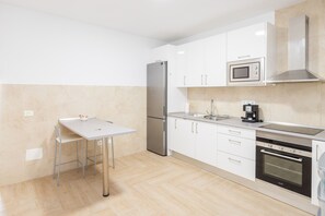 A modern kitchen with white cabinets, a stainless steel refrigerator, a microwave, a coffee maker, and an oven.
