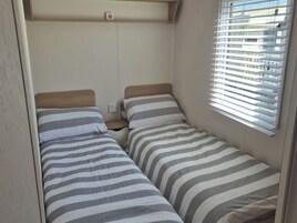 Interior compacto de una caravana con dos camas, una ventana con persianas y un enchufe.