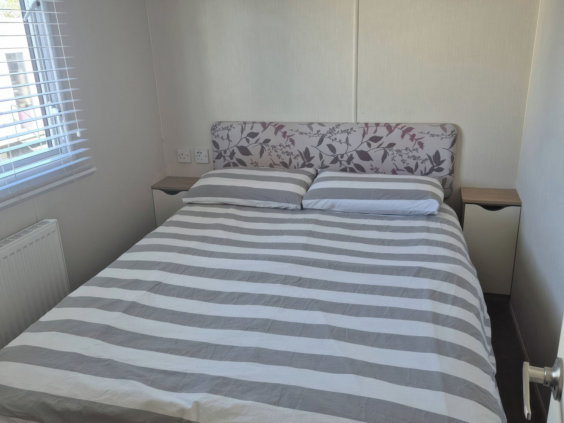 A bed with a striped bedspread, a floral headboard, and two bedside tables.