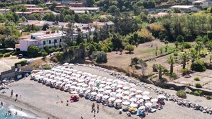 An aerial view of a beach with numerous umbrellas and people, surrounded by residential buildings and greenery. - Amazing home in Piraino (Piraino)