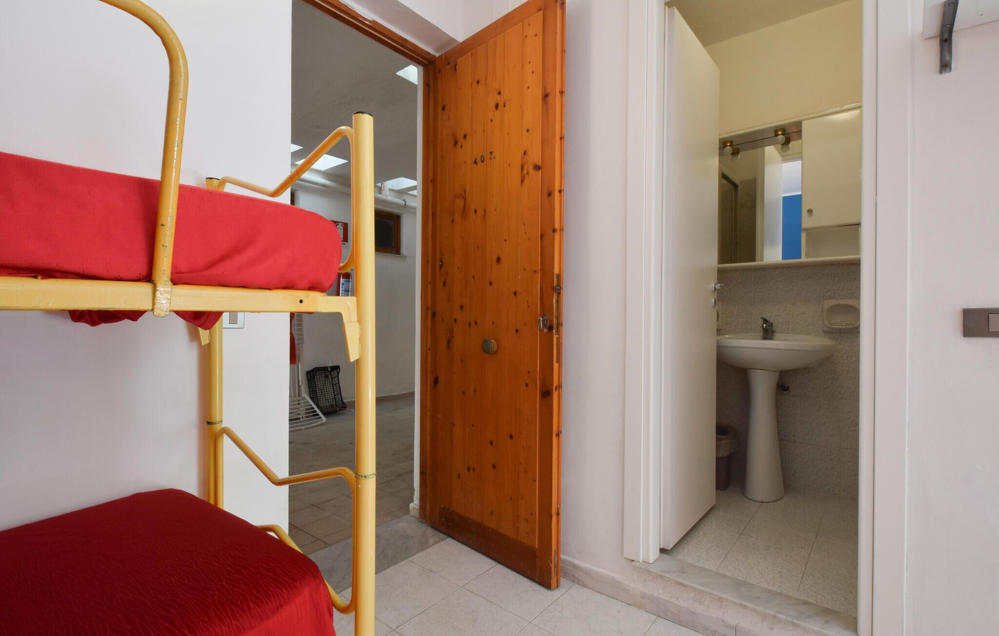A room with a bunk bed, a wooden door, and a bathroom with a sink and mirror.