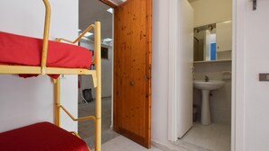 A room with a bunk bed, a wooden door, and a bathroom with a sink and mirror. - Amazing home in Piraino (Piraino)