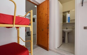 Ein Zimmer mit einem Etagenbett, einer Holztür und einem Badezimmer mit Waschbecken und Spiegel.