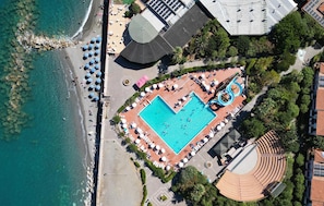 Vista aèria d'un complex turístic amb una gran piscina, una zona de platja i una zona d'estar coberta a l'aire lliure.