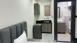 A hotel room with a bed, a small refrigerator, a kitchenette, and a bathroom visible through an open door. - Hotel The Silken Stay By Carlton Suites (Gurugram)