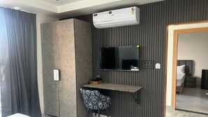 A hotel room with a bed, a desk with a chair, a television, and an air conditioning unit. - Hotel The Silken Stay By Carlton Suites (Gurugram)