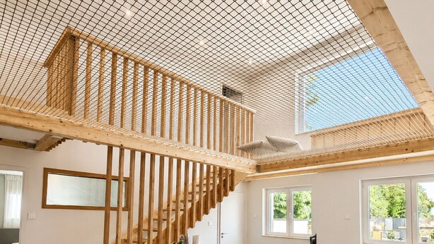 Amplia sala de estar con techo alto, escalera de madera y ventanas grandes.