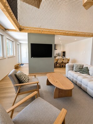 A modern living room with a flat-screen TV, a sofa, a coffee table, and a wooden chair. - Serenity Lodge - Hammock, Nature and Tranquility (Mackenheim)