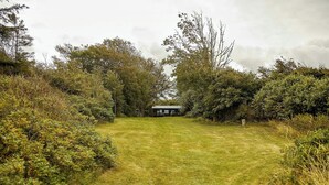 Un camí empedrat travessant una zona verda que condueix a un edifici petit amb teulada inclinada, envoltat de vegetació abundant i arbres.