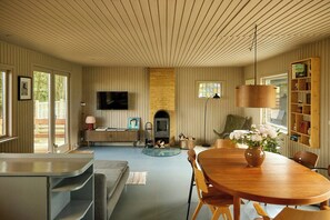 A spacious living room with a fireplace, a television mounted on the wall, and a dining area with a wooden table and chairs.