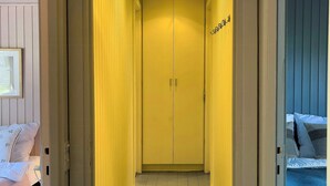 Passadís estret amb una porta tancada al final, flanquejat per dos llits amb roba de llit blanca.