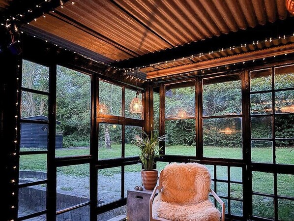 A room with large windows, a wooden ceiling, and a chair with a potted plant.