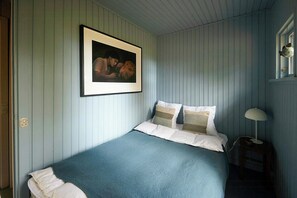 A bedroom with a bed, a framed picture on the wall, and a bedside table with a lamp.