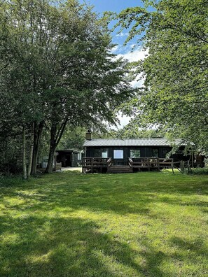 A rustic cabin with a porch, surrounded by lush greenery and trees.