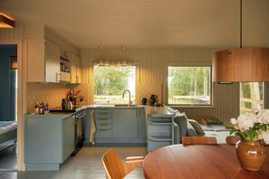 A modern kitchen with a central island, a dining area with a wooden table, and large windows offering views of the outdoors. - Classic 1960s holiday home with Limfjord views (Fur)