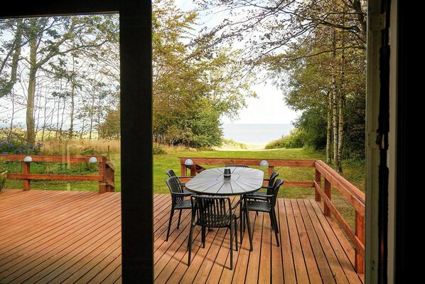 A wooden deck with a round table and chairs, overlooking a beach.