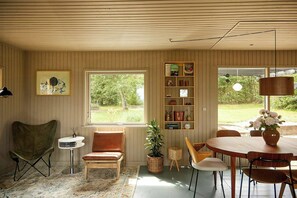 A room with a dining table, chairs, a bookshelf, a potted plant, and a window with a view of greenery.