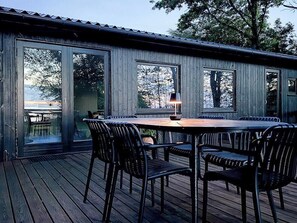 An outdoor deck with a table and chairs, large windows, and a view of trees.