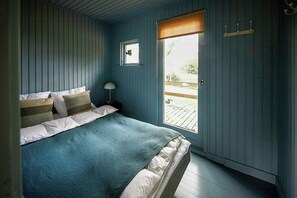 A bedroom with a bed, a nightstand, a lamp, a window with a view of the outdoors, and a door with a coat rack. - Classic 1960s holiday home with Limfjord views (Fur)