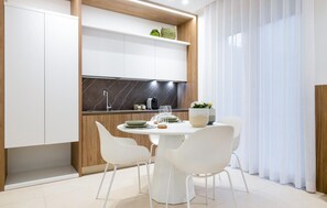 A modern kitchen with white cabinets, a marble backsplash, and a dining area with white chairs and a round table. - Nice apartment in Marina di Ragusa with WiFi (Marina di Ragusa)