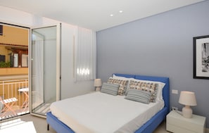 A bedroom with a bed, bedside lamps, a window with curtains, and a balcony with chairs. - Stunning apartment in Marina di Ragusa with WiFi (Marina di Ragusa)