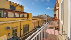 A narrow street with buildings on either side, a parked car, and a balcony with a table and chairs. - Stunning apartment in Marina di Ragusa with WiFi (Marina di Ragusa)
