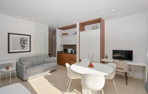 A modern living space with a grey sofa, a white dining table with chairs, a kitchen area, and a television. - Stunning apartment in Marina di Ragusa with WiFi (Marina di Ragusa)