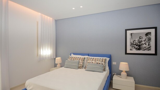 A bedroom with a bed, two bedside tables, a nightstand, a framed picture on the wall, and a window with curtains. - Stunning apartment in Marina di Ragusa with WiFi (Marina di Ragusa)