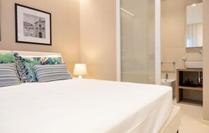 A hotel room with a bed, a nightstand, a lamp, a framed picture on the wall, a bathroom with a sink and mirror. - Stunning apartment in Marina di Ragusa with WiFi (Marina di Ragusa)